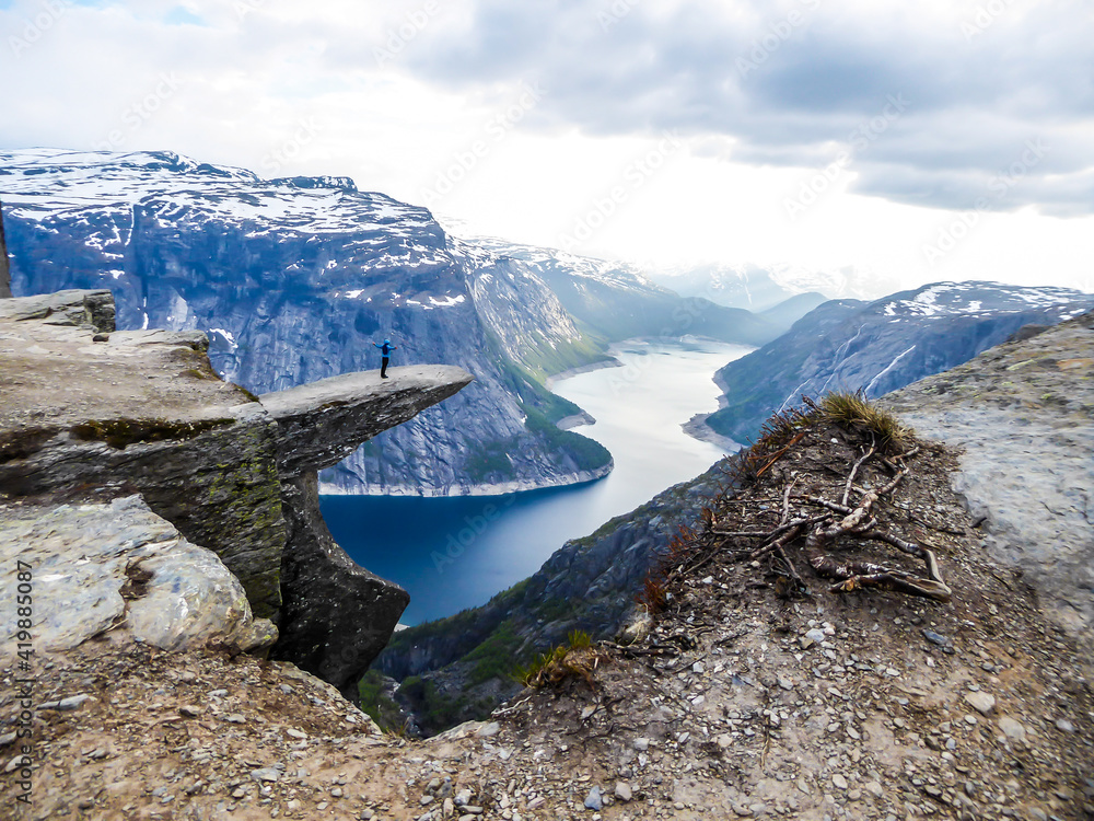 A Man Wearing Blue Jacket Stands At The Hanging Rock Formation Trolltunga With A View On Ringedalsvatnet Lake Norway Slopes Of The Mountains Are Partially Covered With Snow Freedom And Happiness Wall A Man Wearing Blue Jacket Stands At The Hanging Rock Formation Trolltunga With A View On Ringedalsvatnet Lake Norway Slopes Of The Mountains Are Partially Covered With Snow Freedom And Happiness Wall