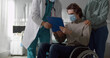 Male patient sitting in wheelchair and wearing safety mask signing discharge paper in hospital