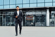 © Тарас Нагирняк - An Indian man in a black suit, a successful manager walks down the street of a modern city, India, behind him modern buildings