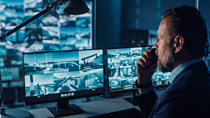 Wall Mural - Male Officer Works on a Computer with Surveillance CCTV Video in a Harbour Monitoring Center with Multiple Cameras on a Big Digital Screen. Employee Uses Radio to Give an Order or Report.