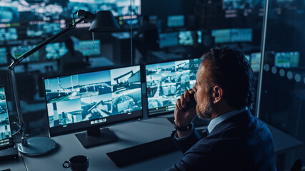 Fototapete - Male Officer Works on a Computer with Surveillance CCTV Video in a Harbour Monitoring Center with Multiple Cameras on a Big Digital Screen. Employee Uses Radio to Give an Order or Report.