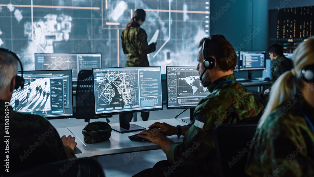Military Surveillance Officer Working on a City Tracking Operation in a Central Office Hub for Cyber Control and Monitoring for Managing National Security, Technology and Army Communications. - obrazy, fototapety, plakaty 