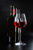 Fototapeta Panele - several different bottles of wine and a glass with red wine on a dark glossy background.