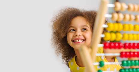 banner of A Black student in a yellow dress laughs brightly behind a colored abacus in an elementary school