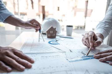 Architects or engineering team consulting and analyzing working on objects tools and construction drawings inspection planning new architectural project on blueprint and model house in modern office