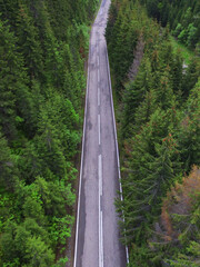 Aerial drone top view of a car driving on a mountainous road, that crosses a spruce forest. Rainy day, the asphalt is still wet. Carpathia, Romania.