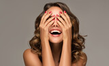 Beautiful woman with curly hair and red nails manicure . Girl happy laughs closes her face with a hand .