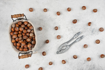 Basket of shelled hazelnuts and nut cracking tool on marble background