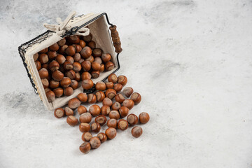 Pile of organic shelled hazelnuts out of basket on marble background