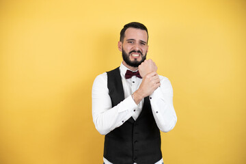 Wall Mural - Young man with beard wearing bow tie and vest suffering pain on hands and fingers, arthritis inflammation