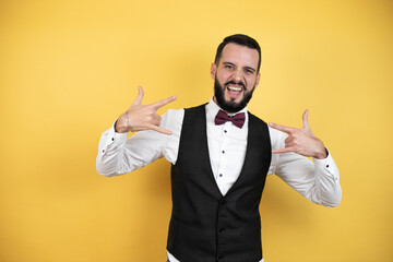 Wall Mural - Young man with beard wearing bow tie and vest Young man with beard wearing bow tie and vest looking confident with smile on face, pointing oneself with fingers proud and happy.