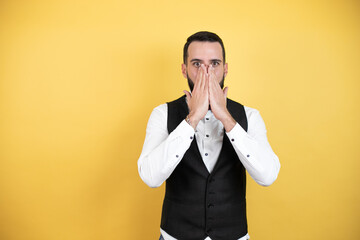 Wall Mural - Young man with beard wearing bow tie and vest shocked covering mouth with hands for mistake. secret concept.