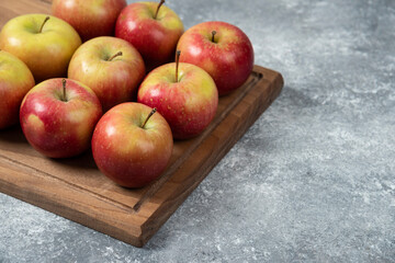 Wooden board of fresh delicious apples on marble surface