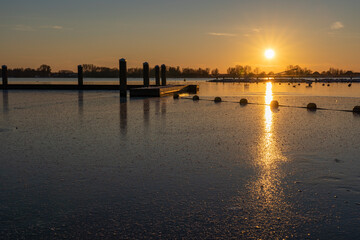 Wall Mural - A colorful sunset at a frozen lake Zoetermeerse Plas with buoys and boat dock in Zoetermeer