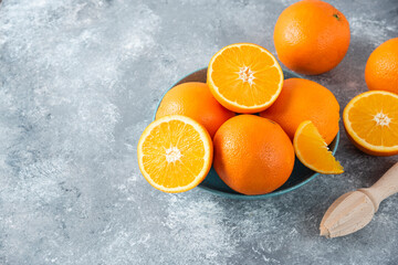 A bowl full of sliced and whole juicy orange fruits with wooden reamer