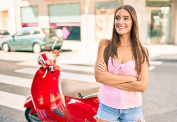 Wall Mural - Young hispanic woman smiling happy standing over scooter at the city