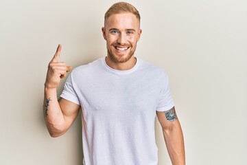 Wall Mural - Young caucasian man wearing casual white tshirt smiling with an idea or question pointing finger up with happy face, number one