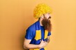 © Krakenimages.com - Redhead man with long beard football hooligan cheering game wearing funny wig with hand on stomach because nausea, painful disease feeling unwell. ache concept.