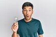 © Krakenimages.com - Young handsome man holding lightbulb for inspiration and idea scared and amazed with open mouth for surprise, disbelief face