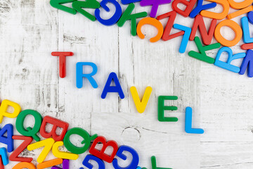 Fototapete - Word - Travel - in bright colorful letters arranged diagonally on grey wood background with corner borders with a multicolored alphabet. Flat lay still life, top view