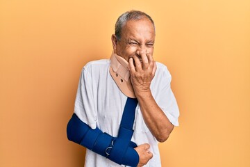 Sticker - Handsome mature senior man wearing cervical collar and arm on sling laughing and embarrassed giggle covering mouth with hands, gossip and scandal concept