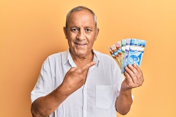 Poster - Handsome mature man holding canadian dollars smiling happy pointing with hand and finger