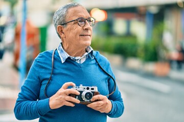Wall Mural - senior grey-haired tourist man smiling happy using vintage camera at the city.