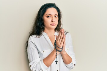 Wall Mural - Beautiful hispanic woman playing with catholic rosary skeptic and nervous, frowning upset because of problem. negative person.