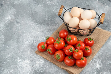 Basket of fresh uncooked eggs and ripe tomatoes on marble background