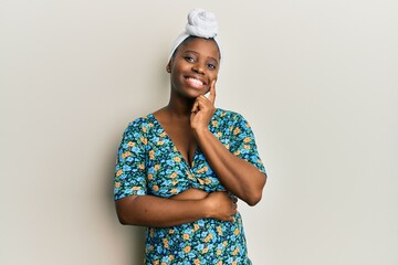 Sticker - Young african woman wearing hair turban and african style looking confident at the camera with smile with crossed arms and hand raised on chin. thinking positive.