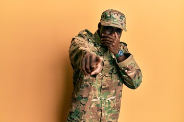 Young african american man wearing army uniform laughing at you, pointing finger to the camera with hand over mouth, shame expression