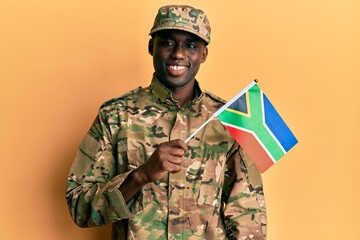 Young african american man wearing army uniform holding south africa flag looking positive and happy standing and smiling with a confident smile showing teeth