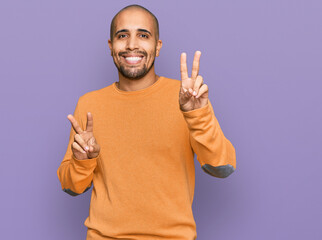 Canvas Print - Hispanic adult man wearing casual winter sweater smiling looking to the camera showing fingers doing victory sign. number two.