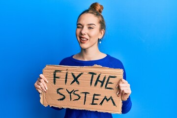 Poster - Young blonde woman holding fix the system banner cardboard winking looking at the camera with sexy expression, cheerful and happy face.