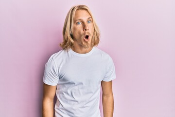 Poster - Caucasian young man with long hair wearing casual white t shirt afraid and shocked with surprise expression, fear and excited face.