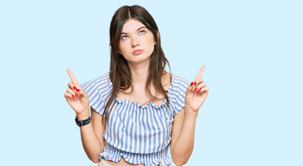 Wall Mural - Young beautiful caucasian girl wearing casual clothes pointing up looking sad and upset, indicating direction with fingers, unhappy and depressed.