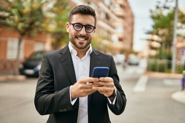 Wall Mural - Young hispanic businessman smiling happy using smartphone at the city.