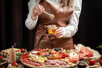 Women's hands holding honey, Antipasto platter. different kinds of cheese and ham, prosciutto, jamon salami