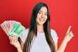 © Krakenimages.com - Young brunette woman holding norwegian krone banknotes smiling happy pointing with hand and finger to the side