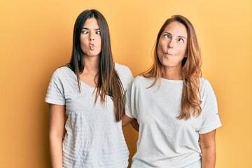 Wall Mural - Hispanic family of mother and daughter wearing casual white tshirt making fish face with lips, crazy and comical gesture. funny expression.