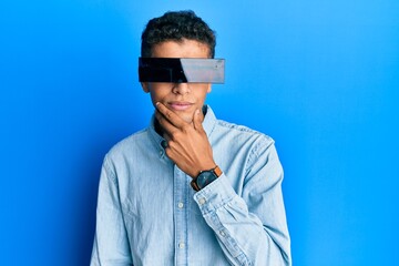 Sticker - Young handsome african american man wearing banner glasses covering eyes serious face thinking about question with hand on chin, thoughtful about confusing idea