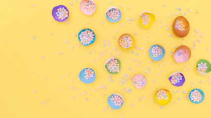 Wall Mural - Top view of yellow backdrop with easter bright hand painted in trendy colors eggshells with colorful foam balls, confetti. Flat lay holiday composition with copy-paste for text postcard, banner