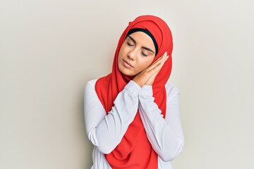 Wall Mural - Young beautiful hispanic girl wearing traditional islamic hijab scarf sleeping tired dreaming and posing with hands together while smiling with closed eyes.