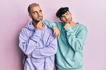 Poster - Homosexual gay couple standing together wearing casual clothes with hand on chin thinking about question, pensive expression. smiling and thoughtful face. doubt concept.