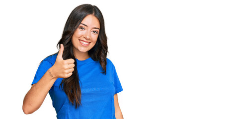 Beautiful brunette young woman wearing casual clothes doing happy thumbs up gesture with hand. approving expression looking at the camera showing success.