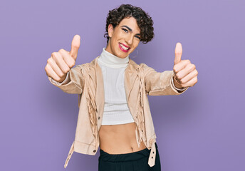 Wall Mural - Handsome man wearing make up and woman clothes approving doing positive gesture with hand, thumbs up smiling and happy for success. winner gesture.