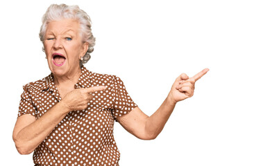 Senior grey-haired woman wearing casual clothes smiling and looking at the camera pointing with two hands and fingers to the side.