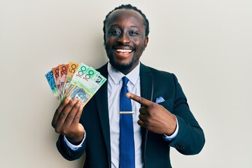 Sticker - Handsome young black man wearing business suit and tie holding australian dollars smiling happy pointing with hand and finger