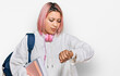 © Krakenimages.com - Hispanic woman with pink hair wearing student backpack and headphones checking the time on wrist watch, relaxed and confident