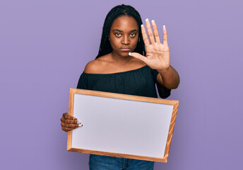 Sticker - Young african american woman holding empty white chalkboard with open hand doing stop sign with serious and confident expression, defense gesture